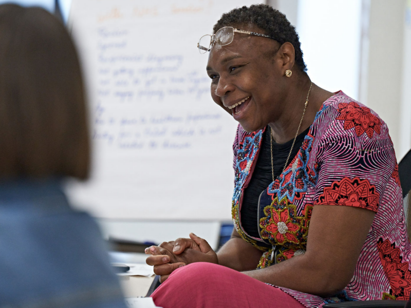 A lady with glasses on sits at a table and smiles during a community event